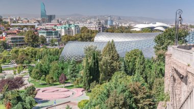 Müzikal Tiyatro ve Sergi Salonu, Gürcistan 'ın başkenti Tiflis' teki Rhike Park 'ın içinde yer almaktadır. Arka planda evler ve gökdelenler