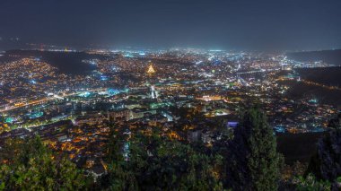 Tiflis şehir manzarası, Gürcistan günden geceye zaman. Şehir merkezinin ve Tiflis 'teki Kura Nehri' nin üst manzarası. Gökyüzünden Gürcistan başkentinin gökyüzü manzarası aydınlatılmış ünlü simgelerle