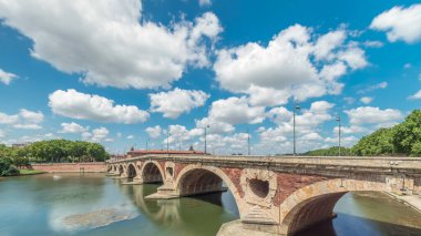 Toulouse, Fransa 'da Garonne Nehri ve Pont Neuf zaman aşımına uğradı. Bu Rönesans kemer köprüsü bulutlu mavi gökyüzünün altındaki suya yansıyor. Yeşil ağaçlı rıhtım