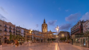 İspanya, Valencia 'daki Plaza de la Reina' da panoramik günden geceye geçiş süreleri aşırı hızlanıyor. Tarihi bir kilise kulesi, hareketli kafeleri ve akşam gökyüzünün altında merkezi bir çeşmesi olan canlı bir meydan..