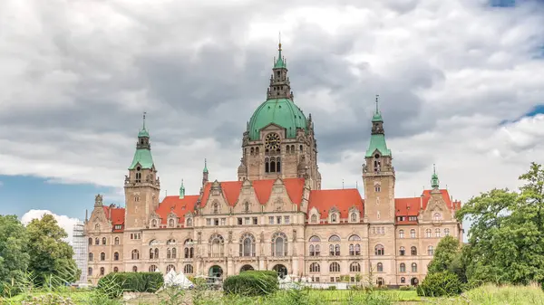 Hanover 'in Yeni Belediye Binası' nın hiperlapesi. Bulutlu bir gökyüzünün altında park ve göl ile çevrili tarihi bir kale gibi bir yapı. Su ve yeşillik üzerindeki yansımalar bu ikonik şehir manzarası zaman çizelgesini oluşturuyor. Almanya