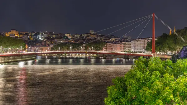 Saone Nehri üzerindeki kırmızı asma köprü ile Lyon 'un şehir manzarasının gece zaman çizelgesi, gece boyunca aydınlatılmış deniz kenarı suya yansıdı. Fransa