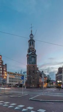 Munttoren Kulesi ve çiçek pazarı. Amsterdam şehir merkezinin panoramik günden geceye geçiş dönemi aşırı hızlanması tramvaylı sokak trafiği. Gün batımından sonra şehir manzarası. Hollanda