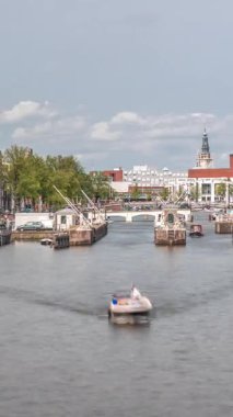 Amstel Nehri 'ndeki Amstel kilitlerinden geçen teknelerin panoramik görüntüsü. Opera binası ve Zuiderkerk kulesi arka planda görünüyor. Bulutlar gökyüzünü dolduruyor. Amsterdam, Hollanda