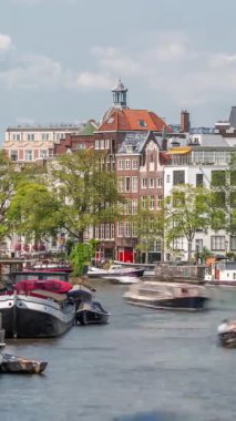 Güneşli bir günde Amsterdams şehir merkezinde yoğun bir nehrin zamanı. Rıhtımı çevreleyen yeşil ağaçlı tekneler trafiği. Arka planda tipik tarihi binalar. Amsterdam, Hollanda