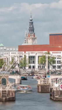 Amstel Nehri 'ndeki Amstel kilitlerinden geçen teknelerin zamanına göre görüntüsü. Opera binası ve Zuiderkerk kulesi arka planda görünüyor. Bulutlar gökyüzünü dolduruyor. Amsterdam, Hollanda