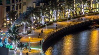 Gece Dubai Marina 'da gezinti zamanı, BAE. Rıhtımda palmiyeler ve kuleler var. Dubai Marina, Dubai 'de yapay kanalı olan bir bölge.