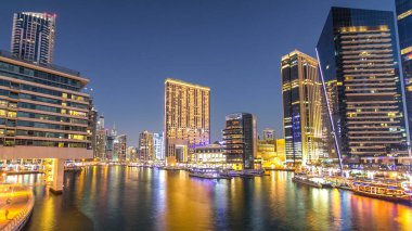 Dubai Marina rıhtımında yatları ve alışveriş merkezi yakınlarındaki modern kuleleri olan Dubai 'de güneş battıktan sonraki gece, Birleşik Arap Emirlikleri. Dubai Marina, Dubai 'de bir şehirdir.
