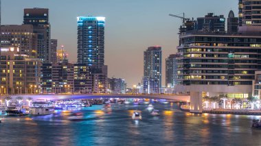 Dubai Marina rıhtımı, Dubai 'deki köprüden gece vardiyasına kadar uzanan kuleleri ve yatları olan Birleşik Arap Emirlikleri. Gün batımından sonra yapay kanallı bölge