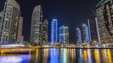 Dubai Marina gezinti güvertesinde yatlar ve modern kuleler Dubai 'deki deniz kıyısından yansıyan su, Birleşik Arap Emirlikleri' nin gece hiperhızlandırması. Yapay kanalla aydınlatılmış bölge