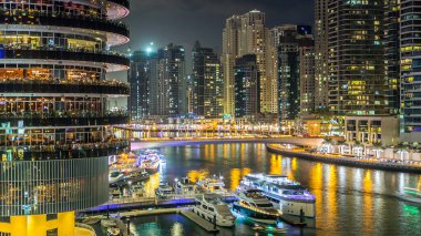 Dubai Marina rıhtımı köprüsü, kuleleri ve yatları Dubai 'deki alışveriş merkezinin balkonundan gece vakti, Birleşik Arap Emirlikleri.