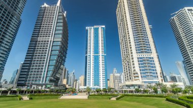 Rıhtımdaki palmiyeli gökdelenlerin hızlandırılmış görüntüsü. Dubai, BAE 'deki parkın yakınındaki Jumeirah Gölü Kuleleri' nde camla kaplı konut binaları. Parktan görüntüle