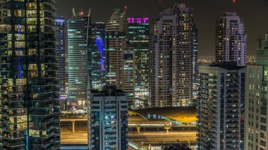 Dubai Marina gezinti güvertesi ve kanalı, Dubai, BAE 'de yüzen yat ve teknelerle dolu. Yanıp sönen ışıkları ve yol trafiği olan aydınlık modern kuleler