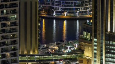 Dubai Marina gezinti güvertesi ve kanalı, Dubai, BAE 'de yüzen yat ve teknelerle dolu. Yanıp sönen ışıkları ve yol trafiği olan aydınlık modern kuleler.