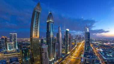 Dubai şehir mimarisi günden geceye geçiş zamanı. Şeyh Zayed yolu üzerindeki aydınlık gökdelenler ve trafik manzaralı üst hava manzarası. Güzel bulutlu gökyüzü. Fisheye merceği