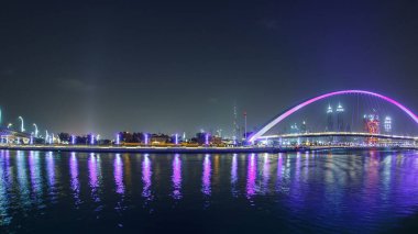 Dubai Su Kanalı 'nın üzerindeki yaya köprüsünün gece gündüz aydınlatılmasıyla Derenin Jumeirah Sahili' ne bağlanması Deira, Downtown ve Safa Parkı 'ndan geçiyor. Gökdelenlerin silueti. Birleşik Arap Emirlikleri