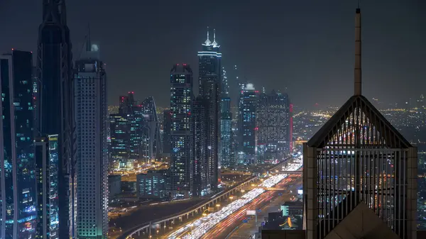 Modern skyscrapers and busy evening highways night timelapse in luxury downtown of Dubai city. Top aerial view from tower rooftop. Dubai, United Arab Emirates