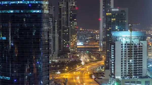 Dubai iş hangarı kuleleri hava gece zaman çizelgesi. Aydınlatılmış bazı gökdelenlerin çatı manzarası ve inşaat halindeki yeni kuleler. Yol kavşağında trafik var.
