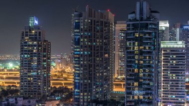 Dubai Marina 'da gece saatlerinde rıhtımda, parlayan ışıklar ve en yüksek gökdelenler. Aydınlatılmış kuleler ve arka plandaki trafik