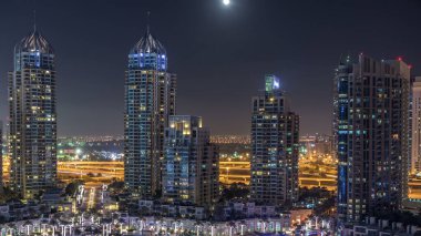Dubai Yat Limanı gece timelapse, Glittering ışıklar ve en yüksek gökdelenler. Işıklı kuleleri ve arka plan üzerinde yolda trafik. Gökyüzüne yükselen ayda