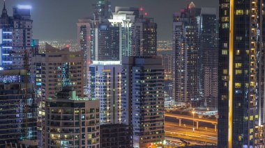 Dubai Yat Limanı ve Jumeirah Lakes Towers gece timelapse, Glittering ışıklar ve en yüksek gökdelenler. İçinde pencere eşiği ve arka plan üzerinde yolda trafik ışık ile aydınlatılmış kuleleri