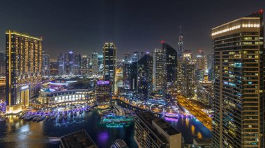 Dubai Marina 'nın gece aydınlatması panoramik zaman ayarlı, BAE. Modern gökdelenler ve konut binaları. Yollarda trafik vardı. Yapay kanal şehrindeki alışveriş merkezinin yakınındaki yatlar ve tekneler.