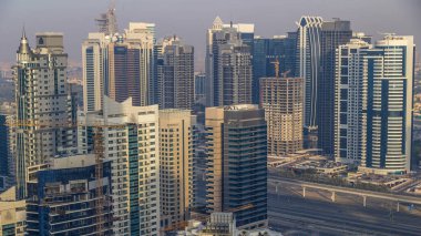 Gün batımında inanılmaz renkli Dubai marinası ve JLT silueti. Otoyolun yakınındaki en yüksek gökdelenlerin büyük perspektifi. Binaların üzerinde güneş ışığı. Birleşik Arap Emirlikleri.