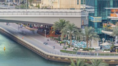 Dubai Marina 'daki gezinti güvertesi ve kanalı, lüks gökdelenleri ve yatları olan, Birleşik Arap Emirlikleri. Köprü yakınında restoranları ve kafeleri olan hava manzaralı.