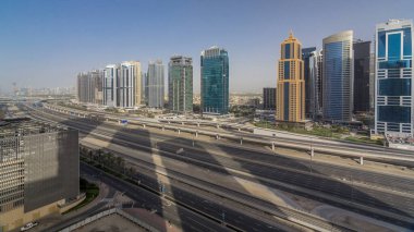 Jumeirah lakes hava görünümünü gökdelenler timelapse Şeyh zayed road ve metro hattı üzerinde trafik ile kuleleri. Günbatımı zamanı uzun gölgeler ve bir cam üzerine düşünceler