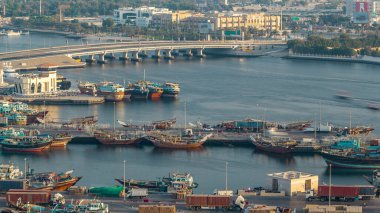 Dubai creek manzara timelapse tekneler ve bağlantı noktası, sakin su ve gün batımı sırasında arka planda modern binalar gemi ile. Hava üstten görünüm yukarıdan trafik ile bir köprü