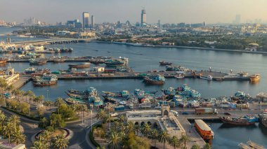 Dubai deresi zaman çizelgesi, limanda tekne ve gemi, sakin su ve günbatımında modern binalar. Yukarıdan gökyüzü panoramik görünümü