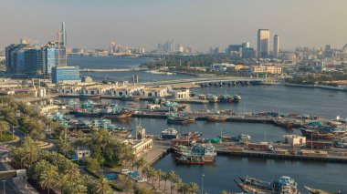 Dubai deresi zaman çizelgesi, limanda tekne ve gemi, sakin su ve günbatımında modern binalar. Yukarıdan yol boyunca trafik ve ağaçlarla hava manzarası