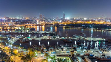 Dubai deresi gece manzarası limanda tekneler ve yatlar ve köprüde trafik olan modern binalar. Yukarıdan gökyüzü panoramik görünümü