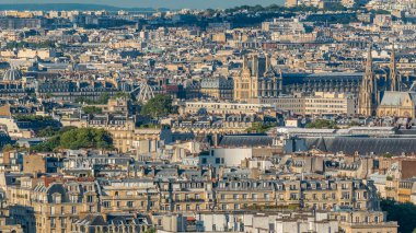 Paris 'teki evlerin çatılarının üstündeki hava manzarası. Müze, katedral kulesi ve gün batımından önce Fransız bayrağıyla akşam manzarası