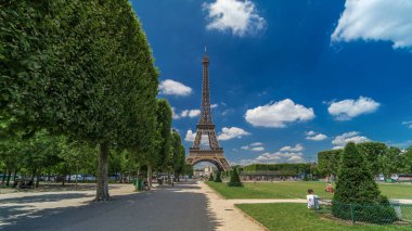 Paris 'teki Champs de Mars' taki Eyfel Kulesi. Zaman atlaması, Fransa. Yazın mavi bulutlu gökyüzü Ağaçlı yeşil çimenler ve etrafta yürüyen insanlar.