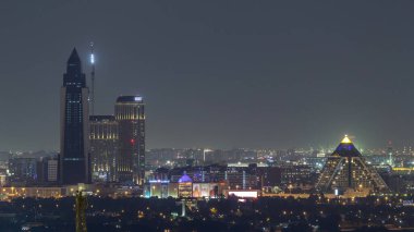 Healthcare City üzerindeki Dubai silüeti ve Dubai, Bae'de gece saatlerinde aydınlatılan piramit. Şehir merkezinden havadan görünüm