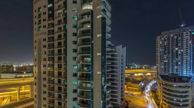 Dubai Marina 'da aydınlık gökdelenler ve gezinti güvertesi gece saatleri. Yol trafiği olan modern kuleler ve tekneler. Birleşik Arap Emirlikleri