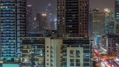 Dubai Marina 'da aydınlık gökdelenler ve gezinti güvertesi gece saatleri. Yol trafiği olan modern kuleler ve tekneler. Birleşik Arap Emirlikleri