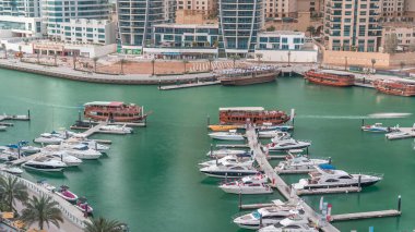 Dubai Marina körfezindeki iskeleye park etmiş lüks yatlar. Şehir hava manzaralı zaman ayarlı. Gezinti geçidi etrafında