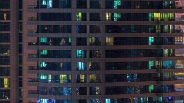 Geceleri apartmanın iç kısımlarında insanlar olan parlak pencereler. Camdan yüzeyi olan modern bir gökdelen. İş ve modern hayat kavramı