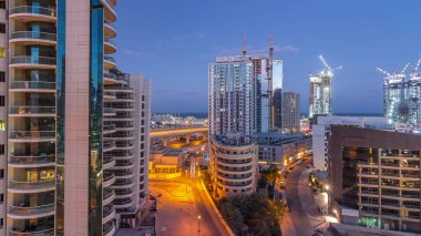 Dubai Marina 'da aydınlık gökdelenler ve gece gündüz gezinti güvertesi geçiş zamanı. Yol trafiği olan modern kuleler ve tekneler. Birleşik Arap Emirlikleri