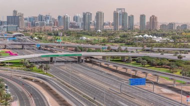 Dubai Golf Sahası 'nın arka planında yeşil ve tekom bölgelerinden oluşan bir şehir manzarası var. Şeyh zayed yolunda trafik kesişiyor.