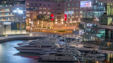 Dubai Marina Limanı 'ndaki rıhtım güvertesi gece uçuşları. Kanalda yüzen tekne ve yatlar. Dubai, Birleşik Arap Emirlikleri