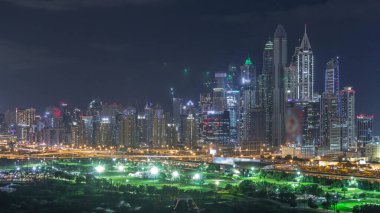 Dubai Marina, Dubai, Birleşik Arap Emirlikleri'nde gece saatlerinde gökdelenleri ve golf sahalarını aydınlatmaktadır. Yeşiller bölgesinden havadan görünüm