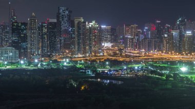 Jumeirah göl kuleleri ve Dubai marina aydınlatılmış gökdelenler ve golf sahası gece timelapse, Dubai, Birleşik Arap Emirlikleri. Yeşiller bölgesinden havadan görünüm