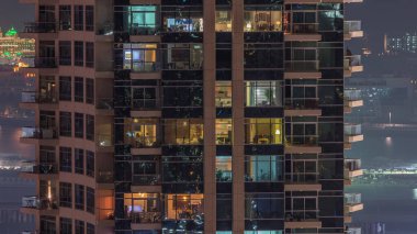 Geceleri apartmanın iç kısımlarında insanlar olan parlak pencereler. Camdan yüzeyi olan modern bir gökdelen. İş ve modern hayat kavramı