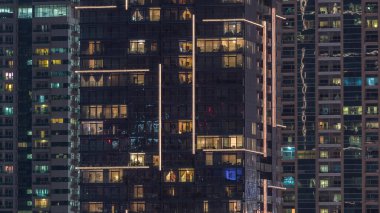 Geceleri apartmanların iç kısımlarında insanlar olan parlak pencereler. Camdan yüzeyi olan modern gökdelenler. İş ve modern hayat kavramı. Eğil.