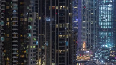 Dubai Marina konutlarının ve ofis gökdelenlerinin pencerelerinde ışıklar ve deniz kıyısında gece saatleri olan hava manzarası. Yüzen tekneler ve yatlar