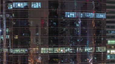 Ofis gökdeleni gece geç saatlerde iç ışıklar açıkken ve insanlar gece vardiyasında çalışırken. Yukarıdan birçok pencereye sahip havadan yakın görüntü