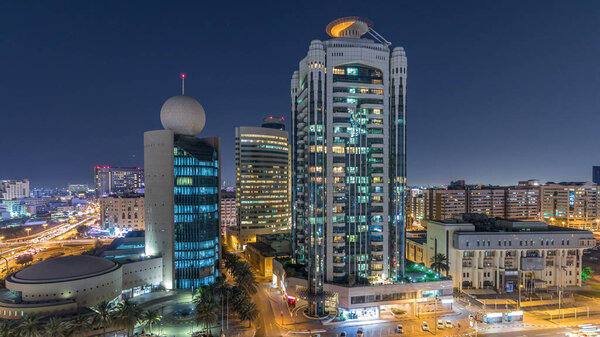 Район Дубай Крик, окруженный современными зданиями и оживленным движением улиц в ночное время. Верхний вид сверху с подсветкой небоскребов